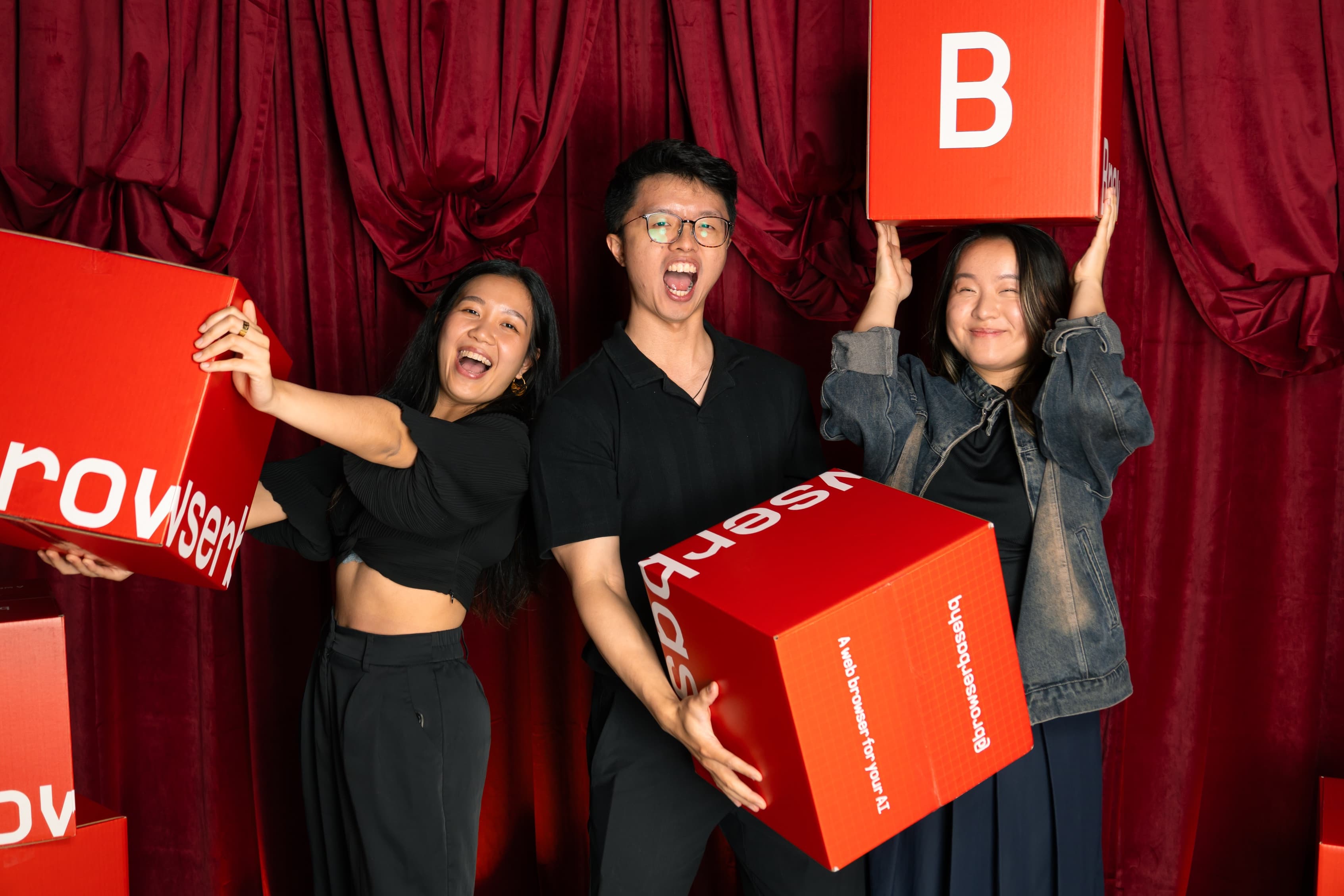 Three guests posing with oversized red Browserbase B boxes in front of a red curtain